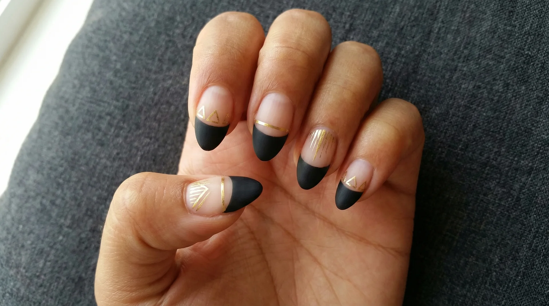 Almond nails with black french tip and fine hand-painted gold geometric lines on nail body