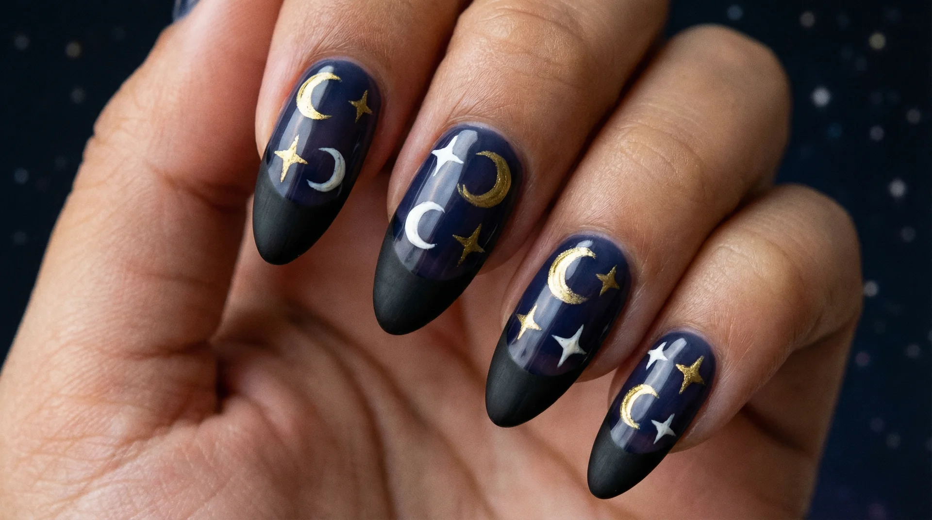 Almond nails with black french tip and scattered gold crescent moons and stars on navy base