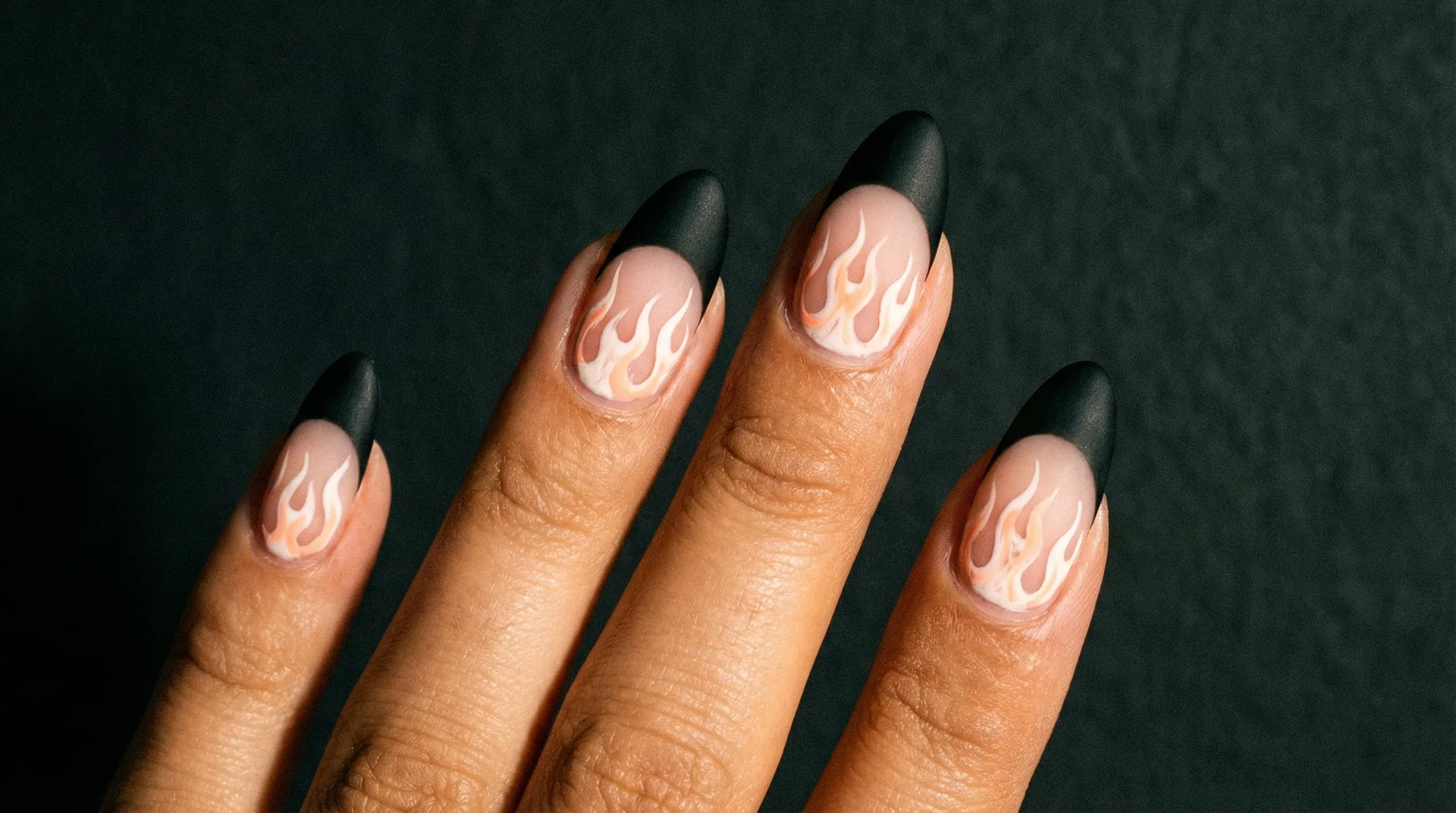 Almond nails with black french tip and small stylized flame nail art on nail body
