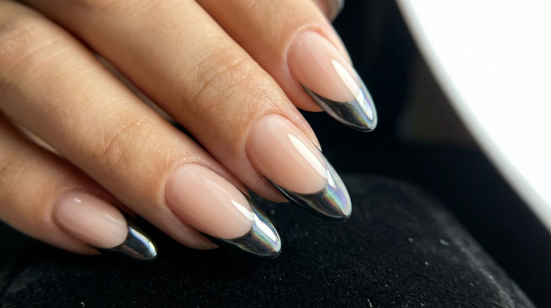 Almond nails with chrome reflective black french tip under directional studio lighting