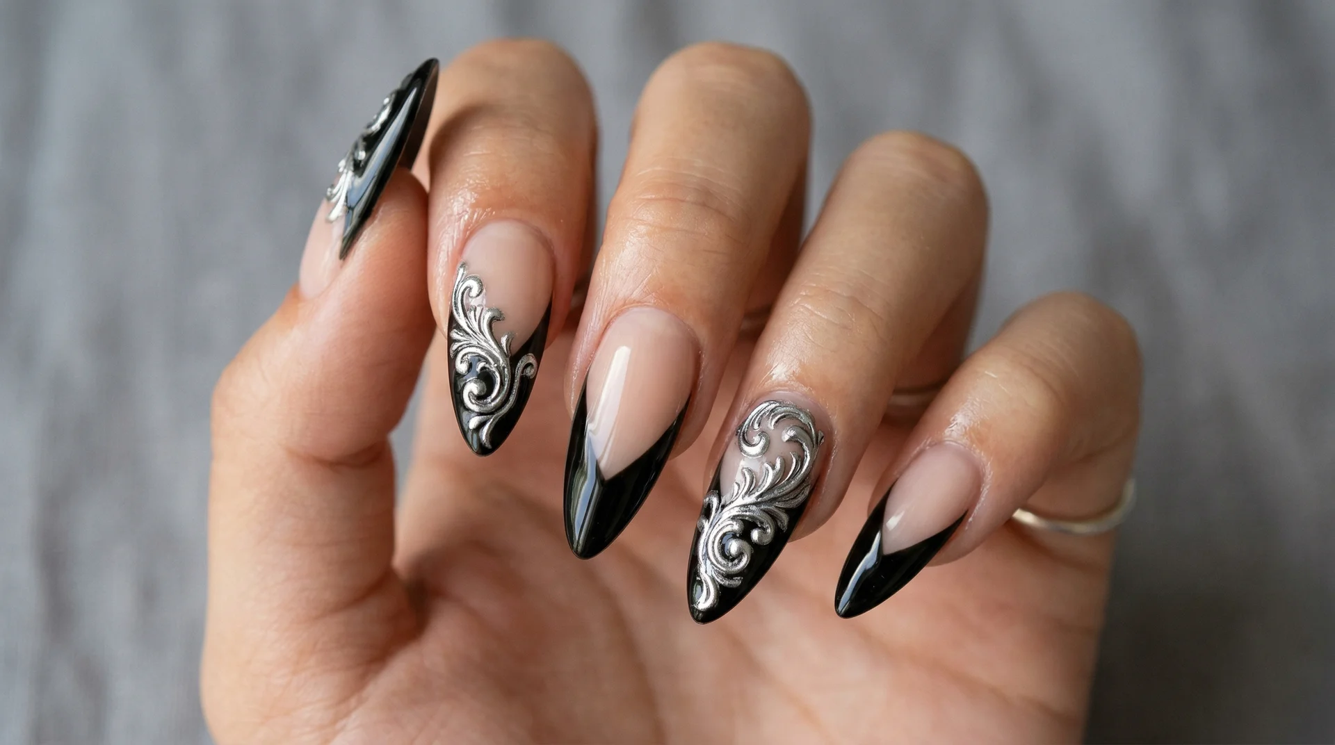 Almond nails with dramatic black V-tip and raised silver baroque scroll detail in relief