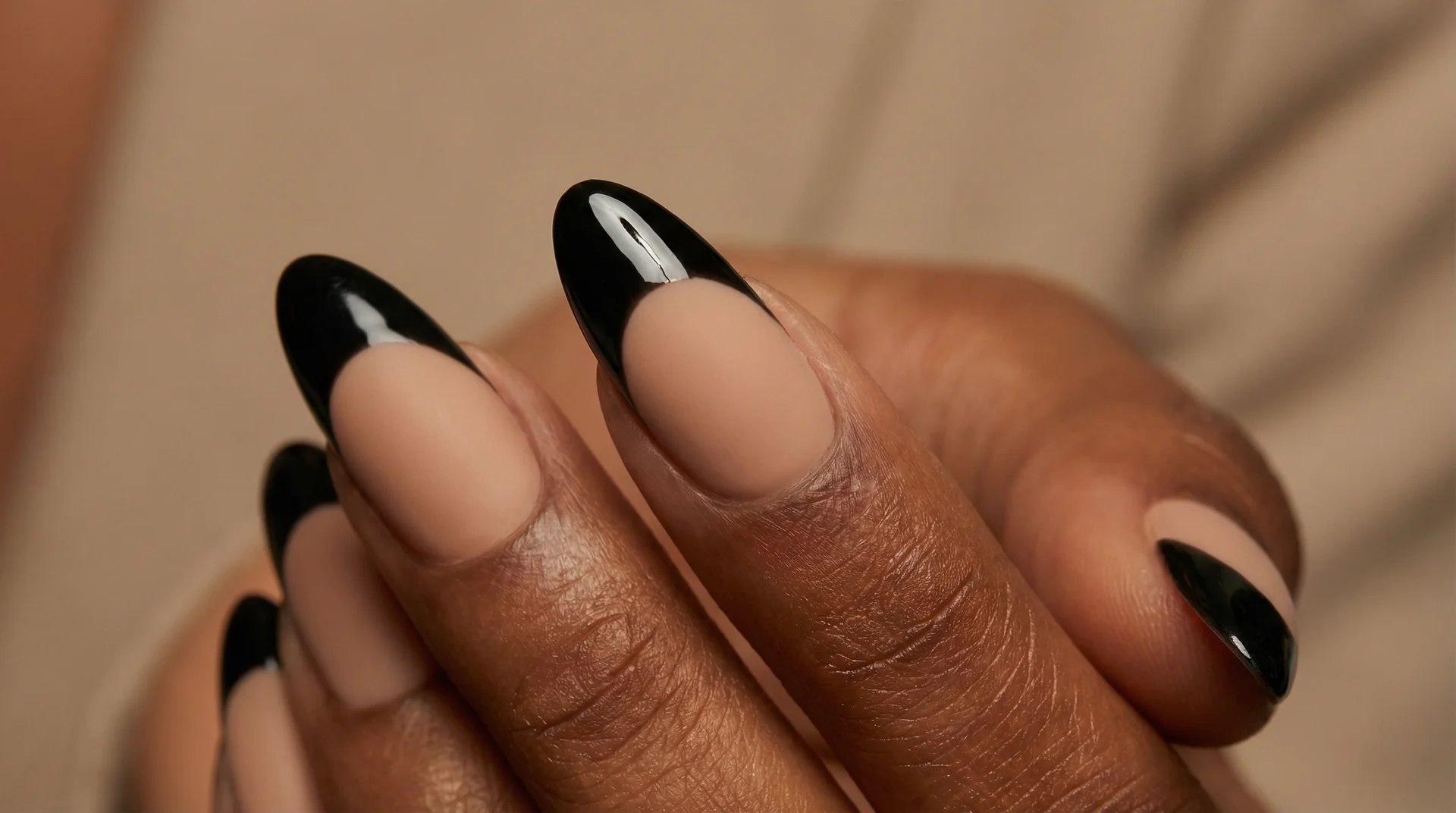 Almond nails with glossy black french tip on warm nude beige base under studio lighting