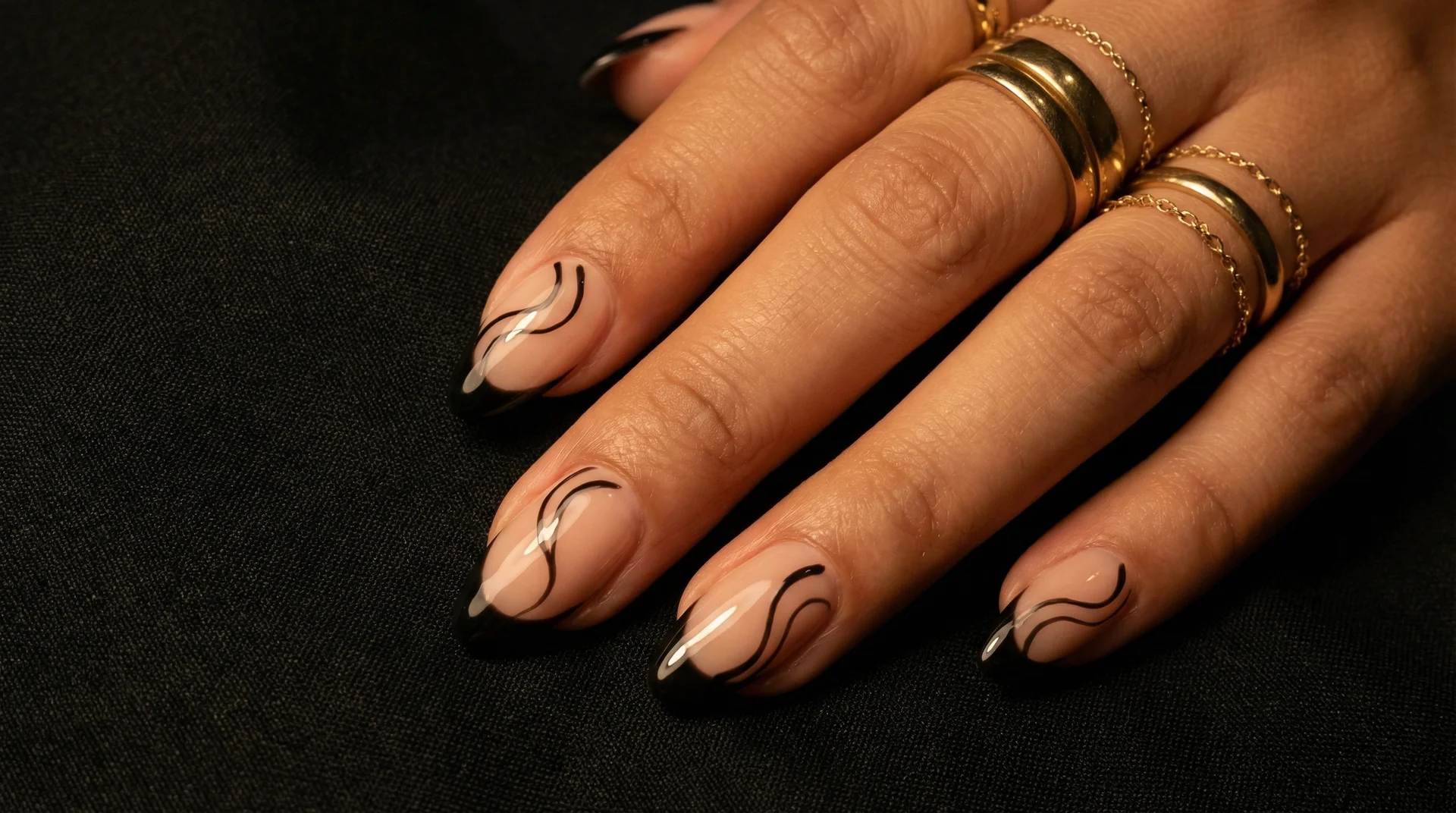 Almond nails with glossy black tip and flowing hand-painted black swirl lines on nude base