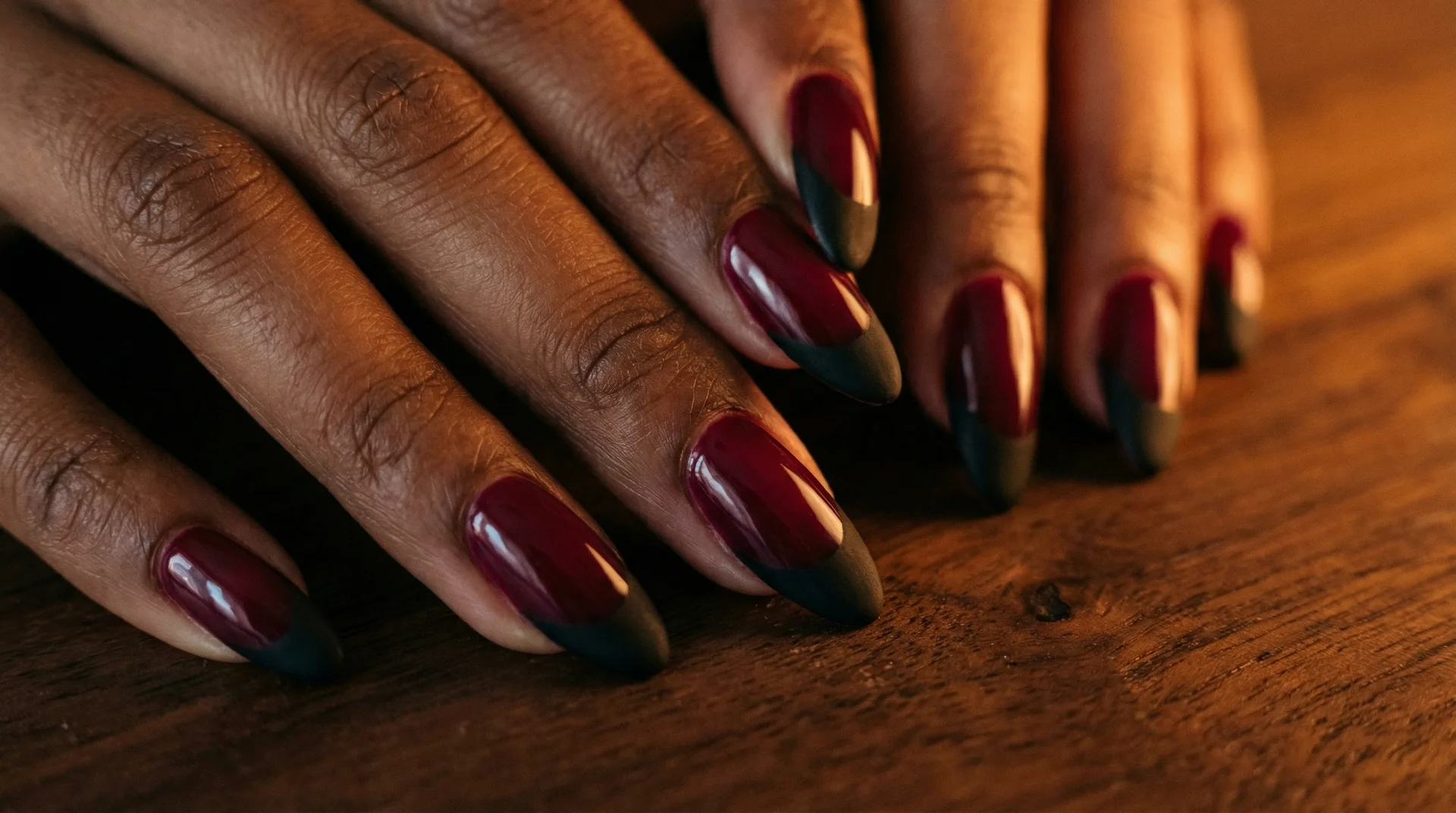 Almond nails with matte black french tip on deep burgundy glossy base on dark wood