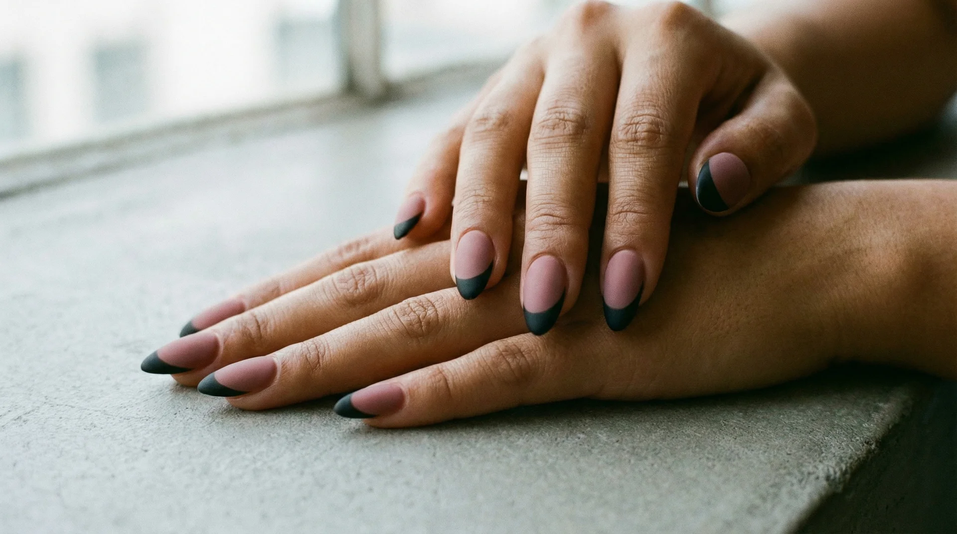 Almond nails with matte black french tip on dusty muted mauve base in diffused lighting