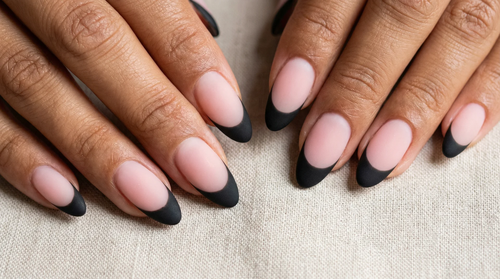 Almond nails with matte black french tip on sheer pink base in natural daylight