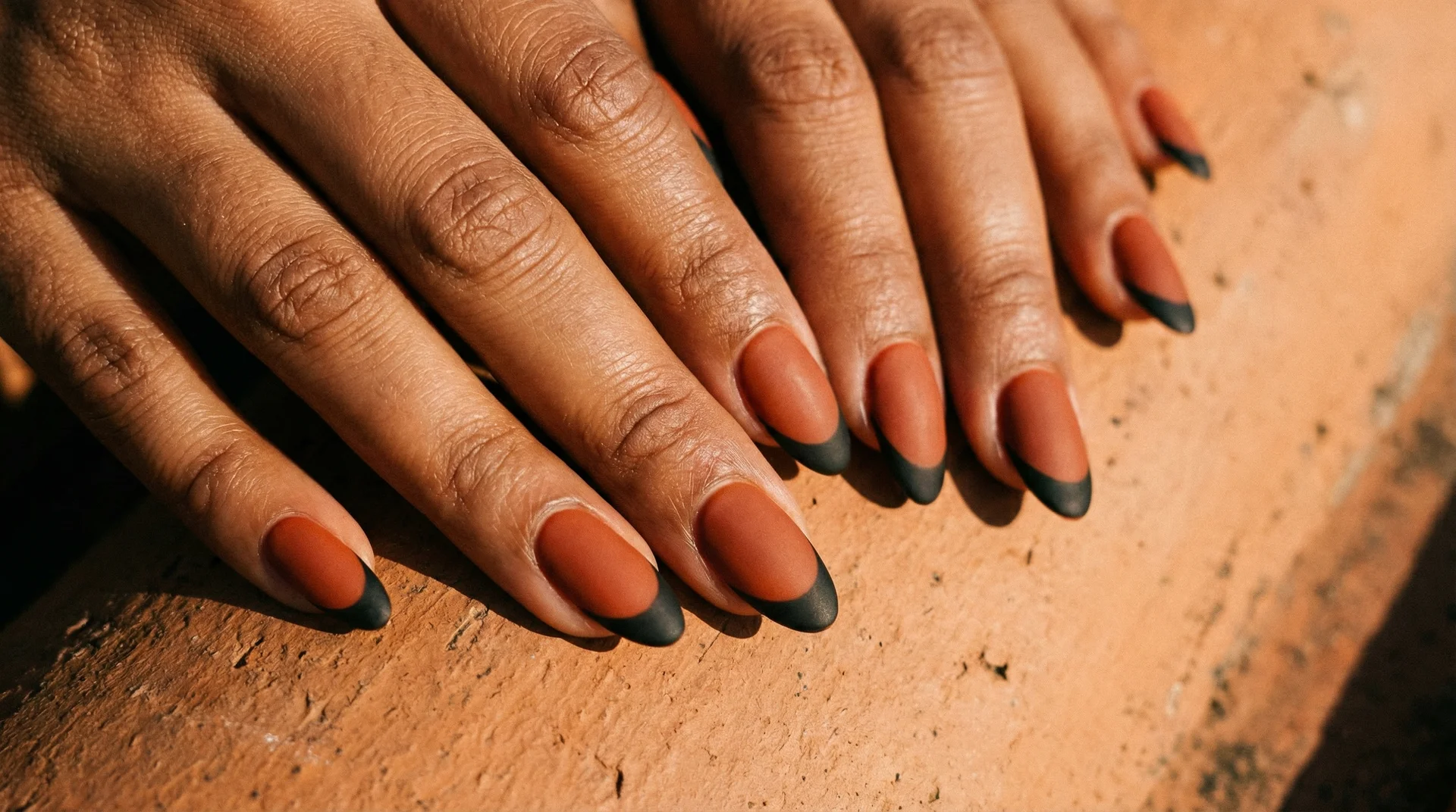 Almond nails with matte black french tip on warm terracotta clay base in natural light
