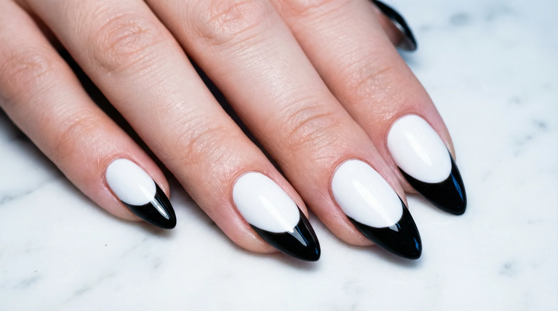 High-contrast almond nails with black tip on stark white base on marble surface