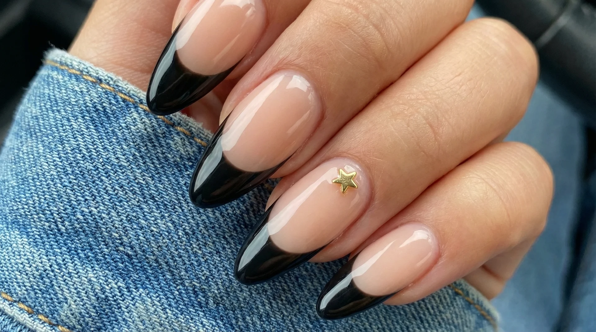Long almond nails with wide black french tip on sheer nude base and gold star charm accent