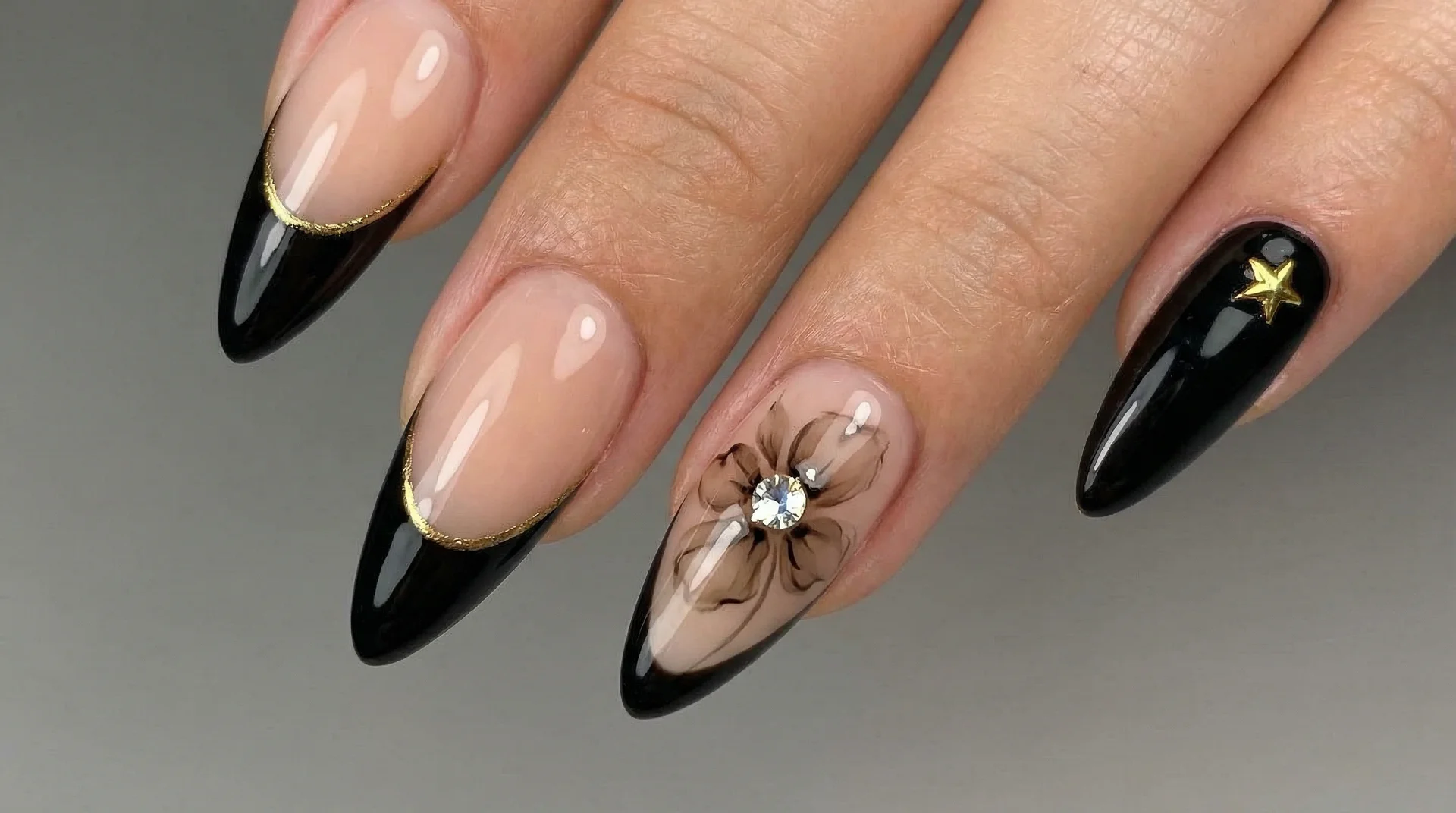 Mixed almond nail set with black gold-lined tips, sheer botanical flower accent, and star charm