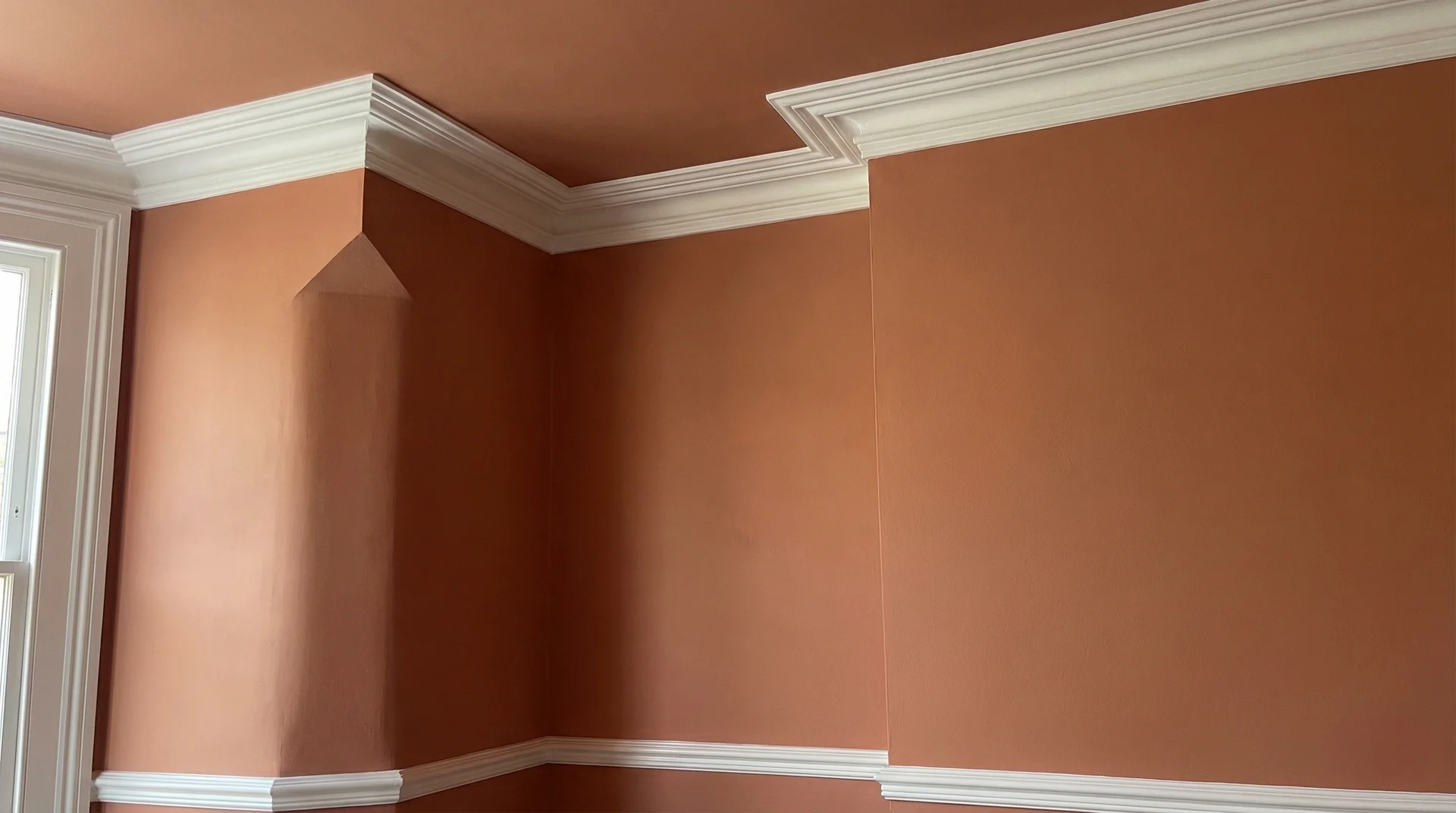 Room corner with matching terracotta walls and ceiling, with white crown molding trim providing a crisp visual boundary