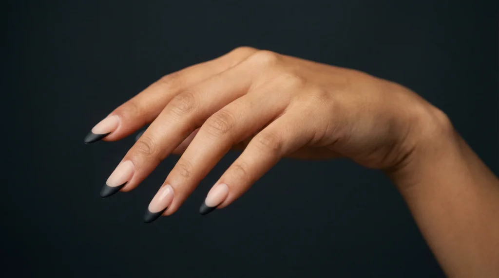 Woman's hand with long almond nails featuring matte black french tips on sheer nude base