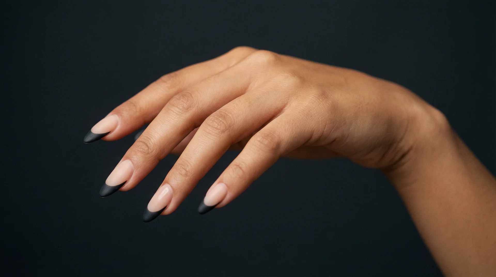 Woman's hand with long almond nails featuring matte black french tips on sheer nude base