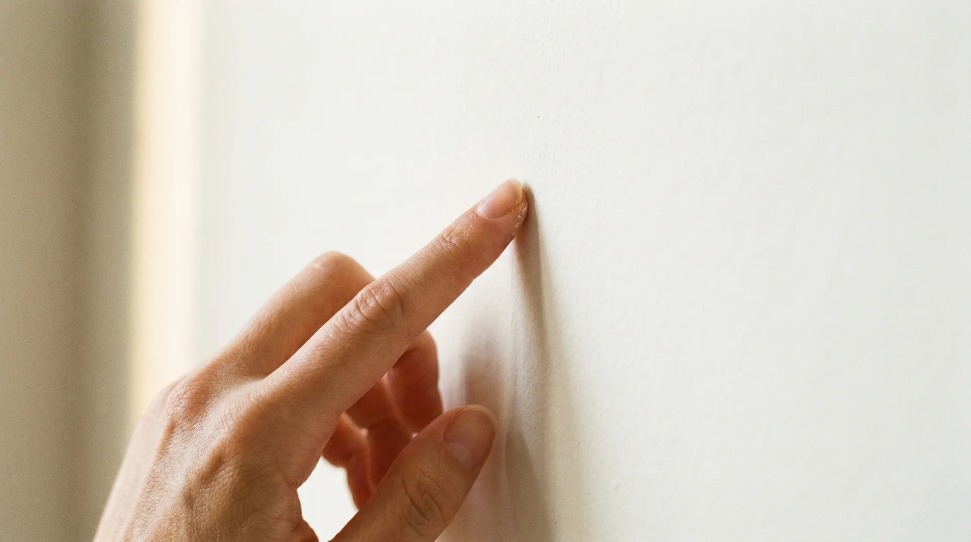 A finger gently pressing against a freshly painted wall to test if the surface is dry and ready for a second coat