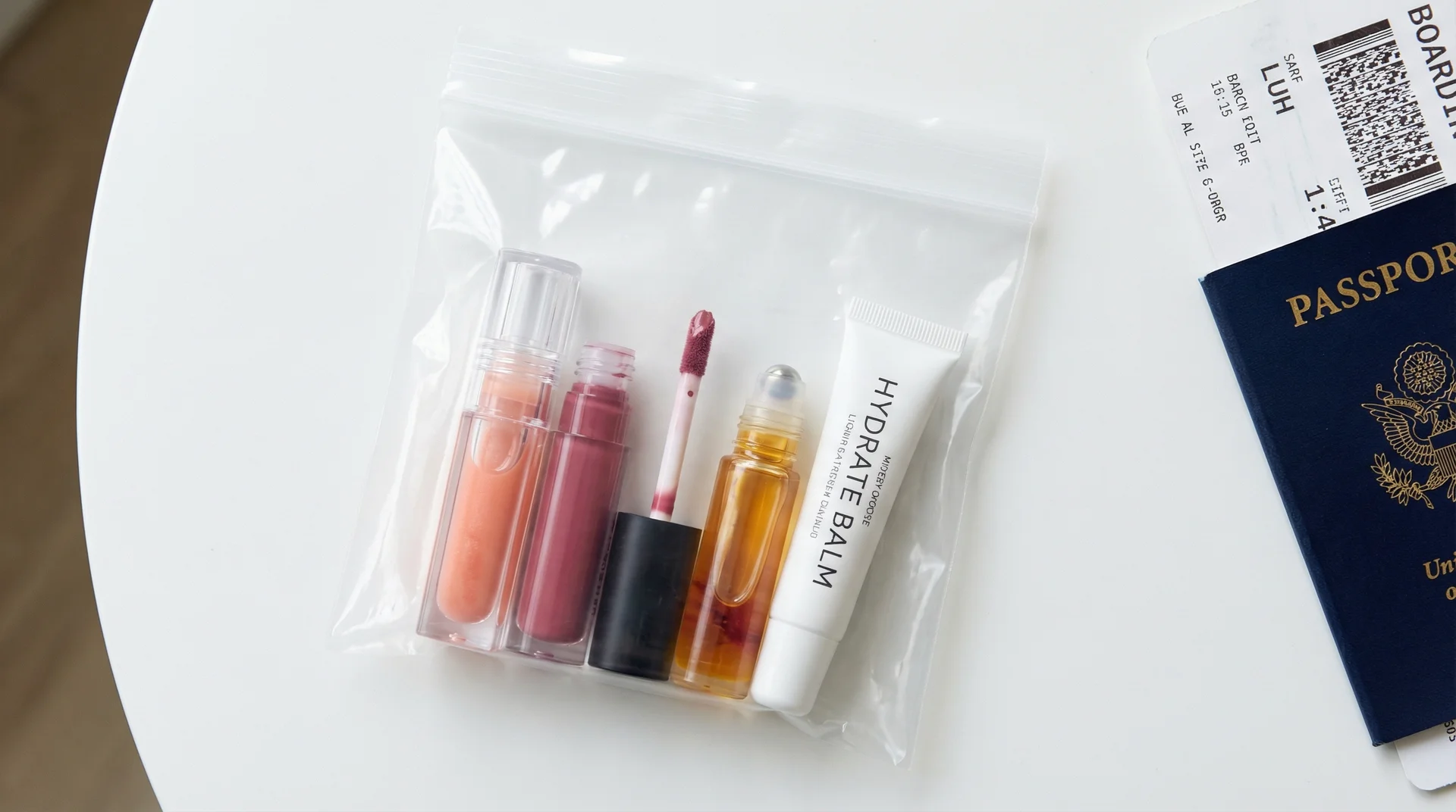 Clear TSA quart bag containing lip gloss, liquid lipstick, lip oil, and squeeze tube balm for carry-on travel
