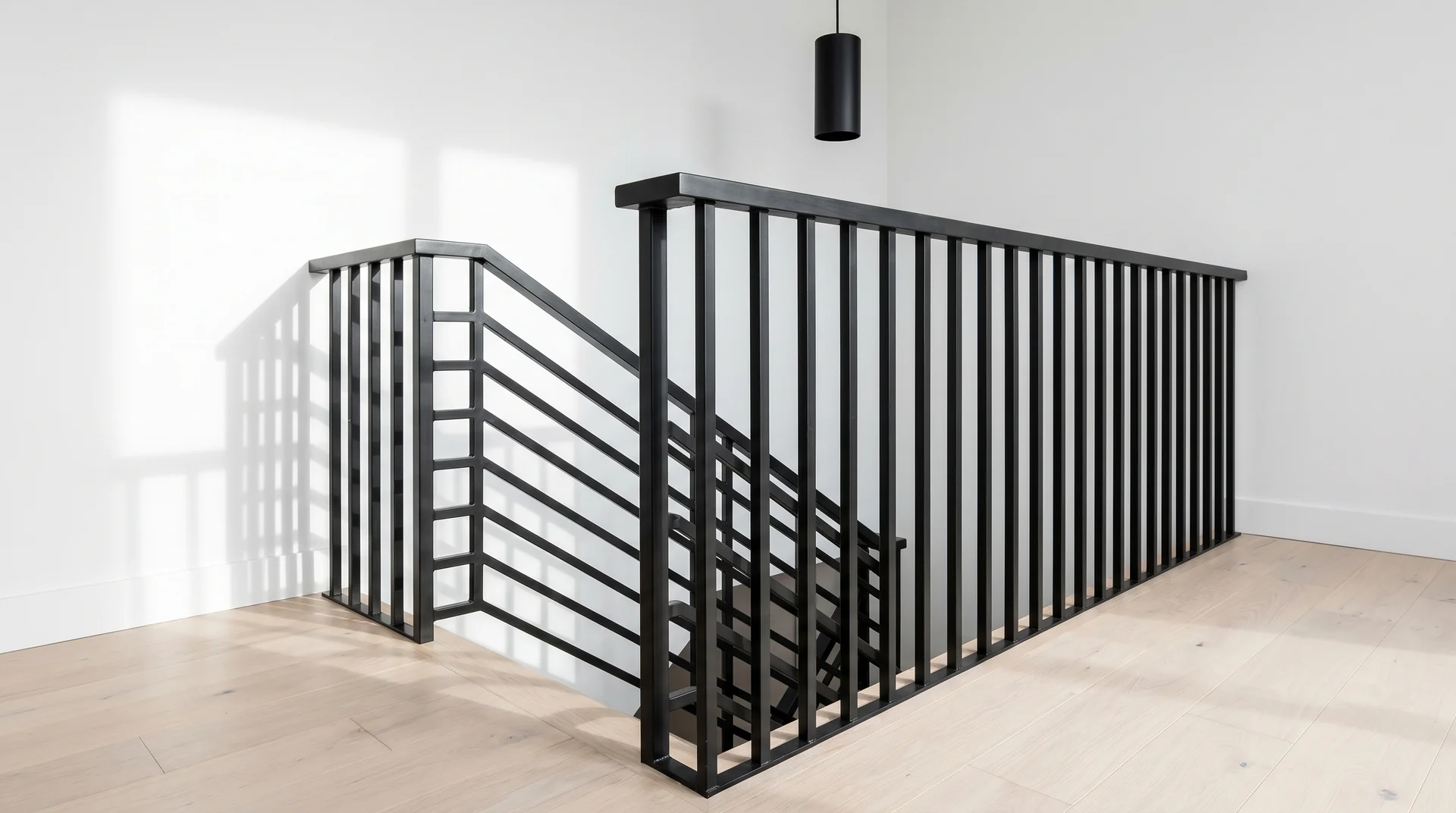 Contemporary staircase with an all-black painted railing against bright white walls and pale blonde wood floors 