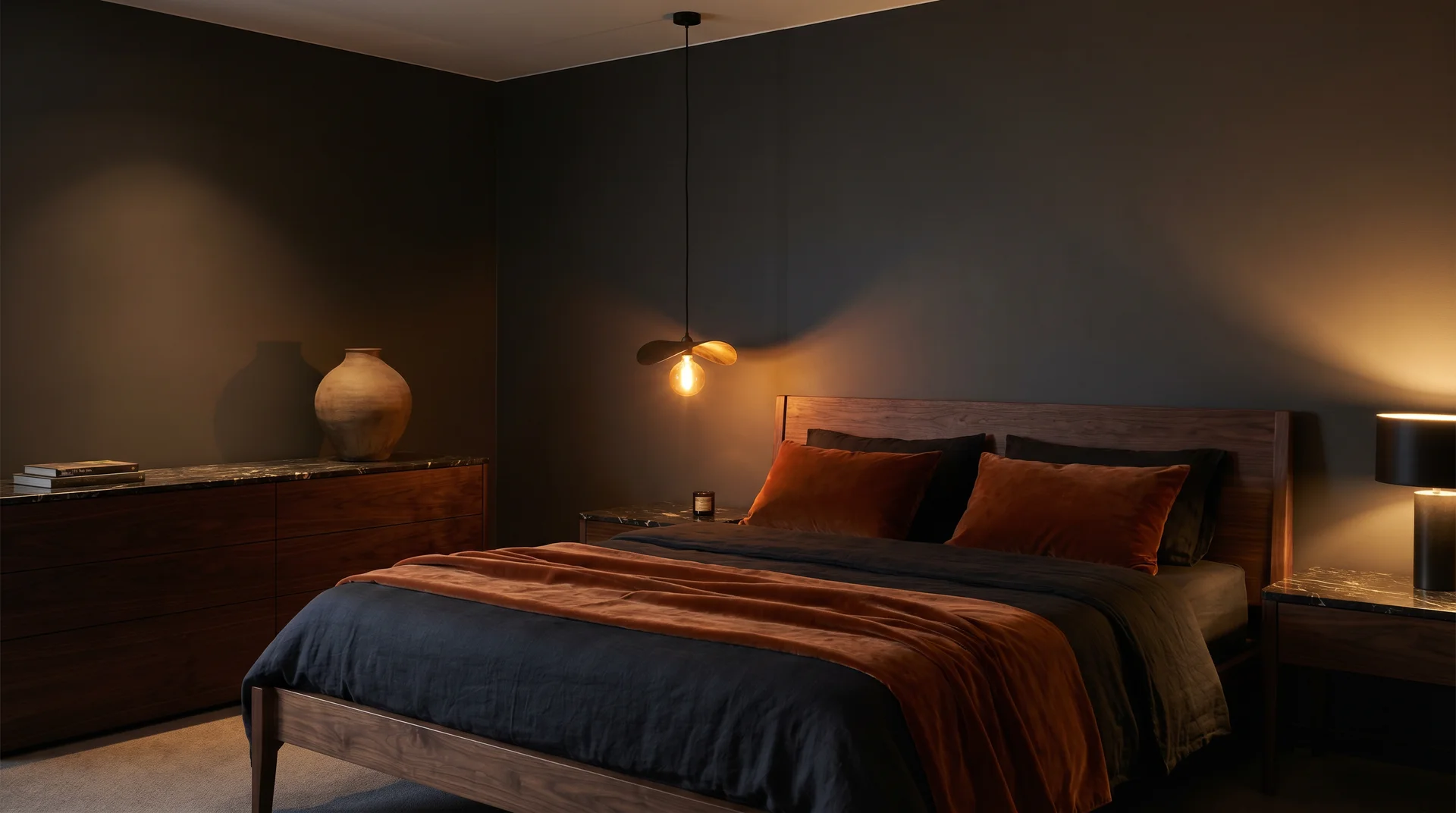 Dark boutique hotel bedroom with burnt orange accents, dark marble surfaces, walnut bed, and pendant light