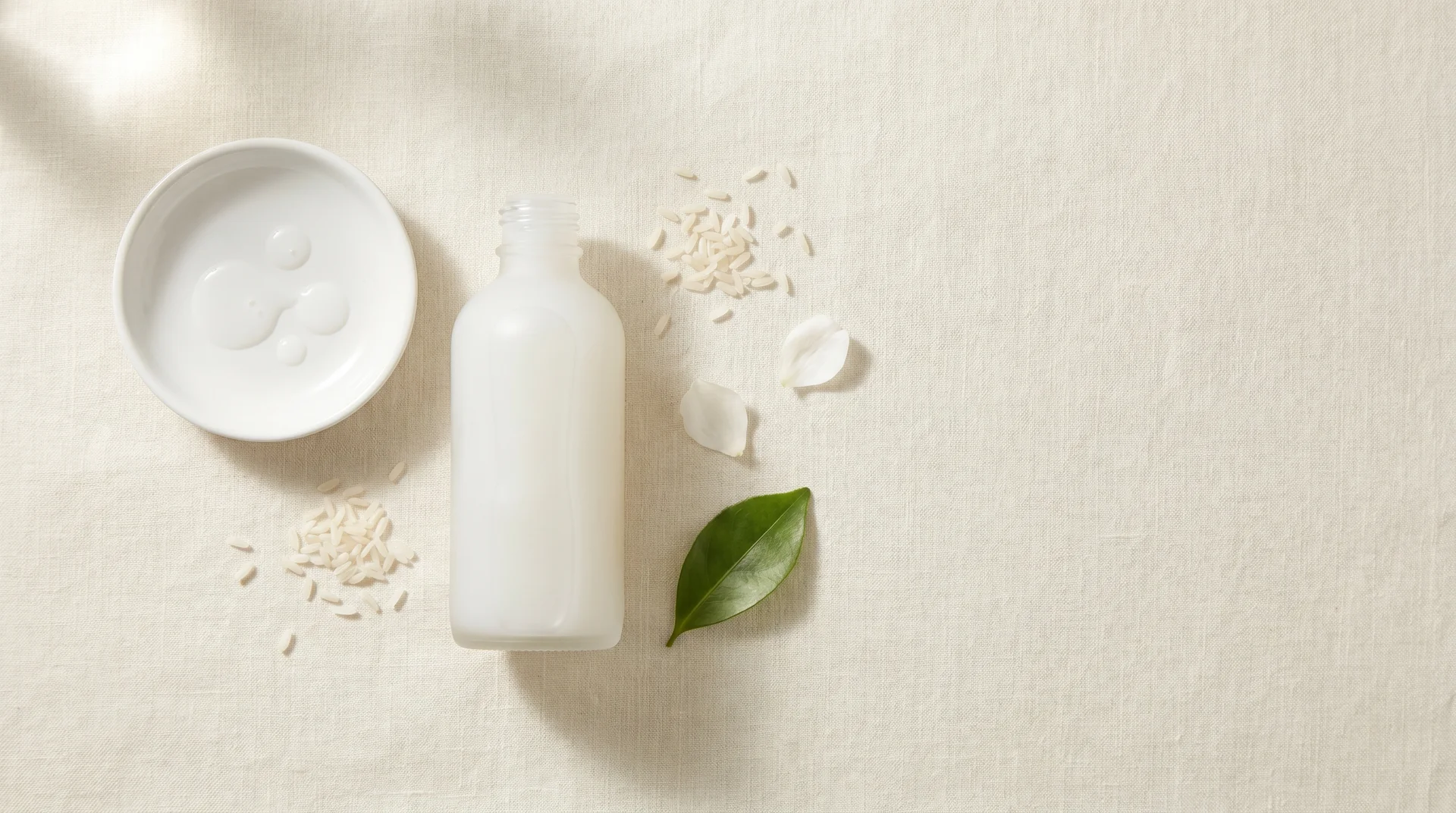 Frosted glass Korean milky toner bottle with rice grains and botanicals on cream linen