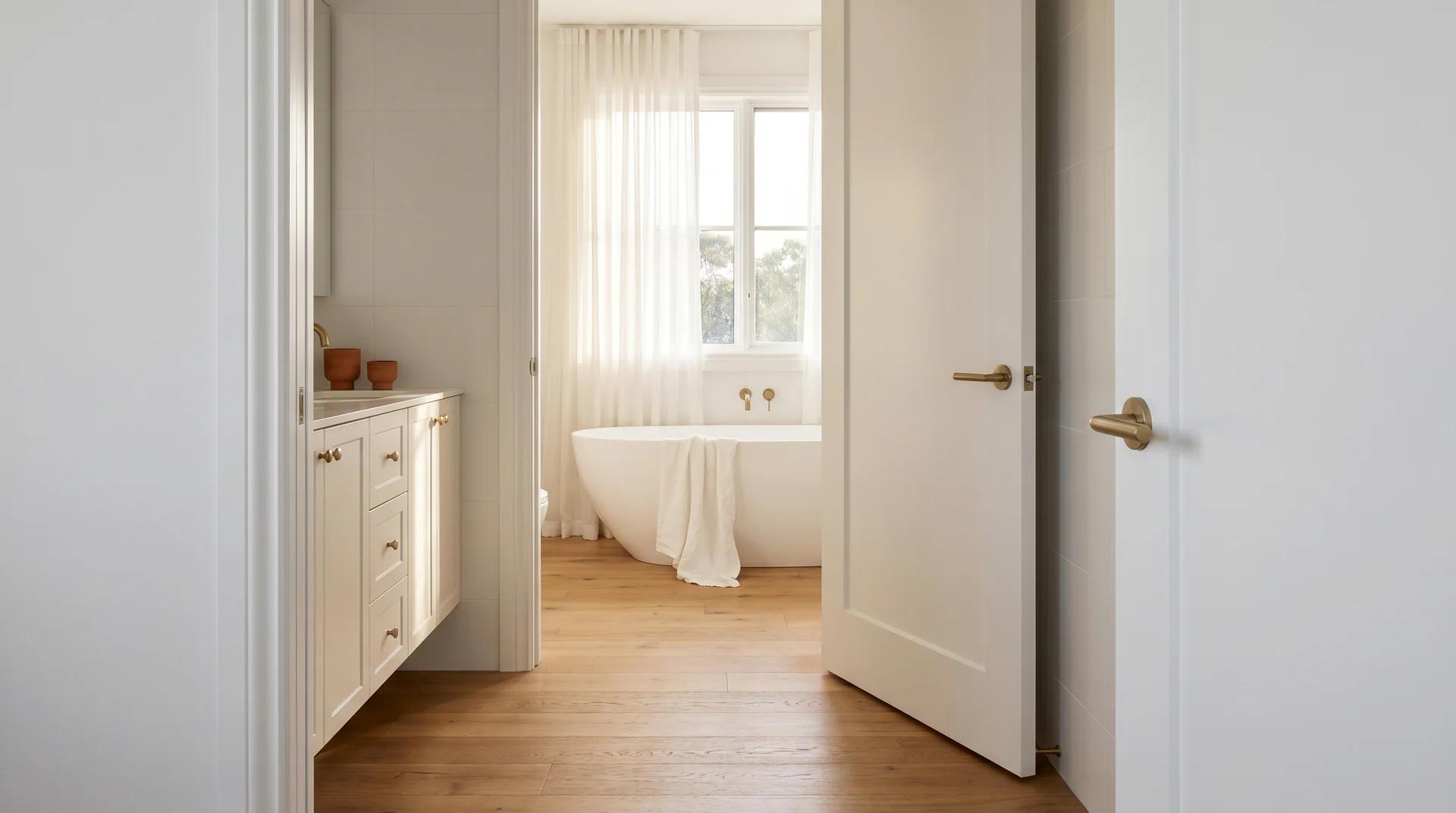 Primary bathroom viewed through a wide open door showing a freestanding tub, double vanity and warm spa-like interior