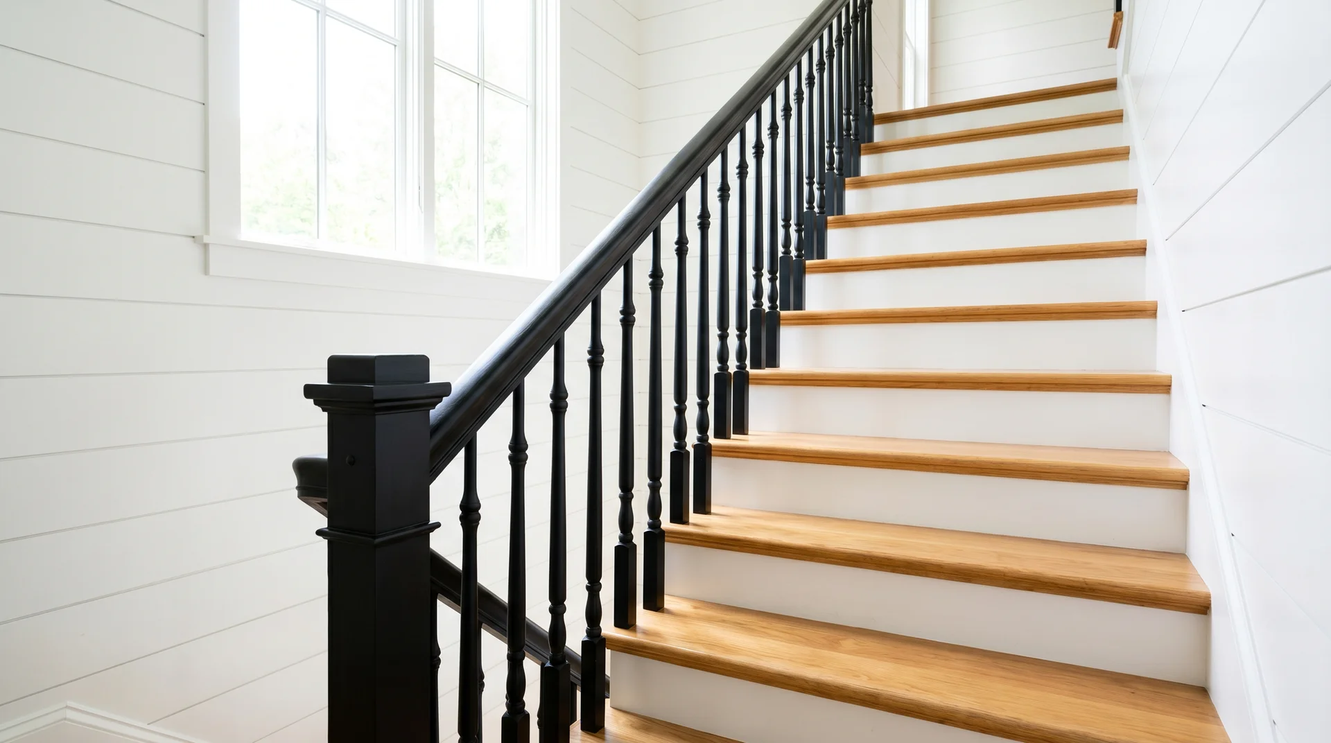 Traditional staircase with natural oak treads and white risers featuring black painted spindles, handrail, and newel post