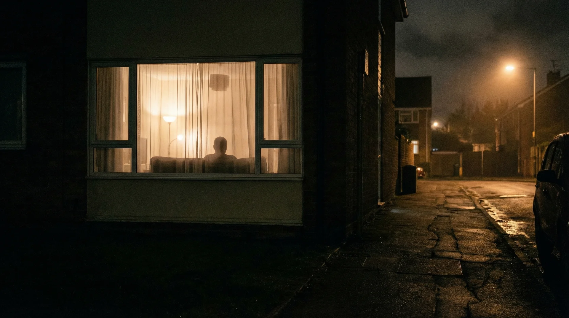 View from outside at night showing a silhouette visible through lit sheer curtains