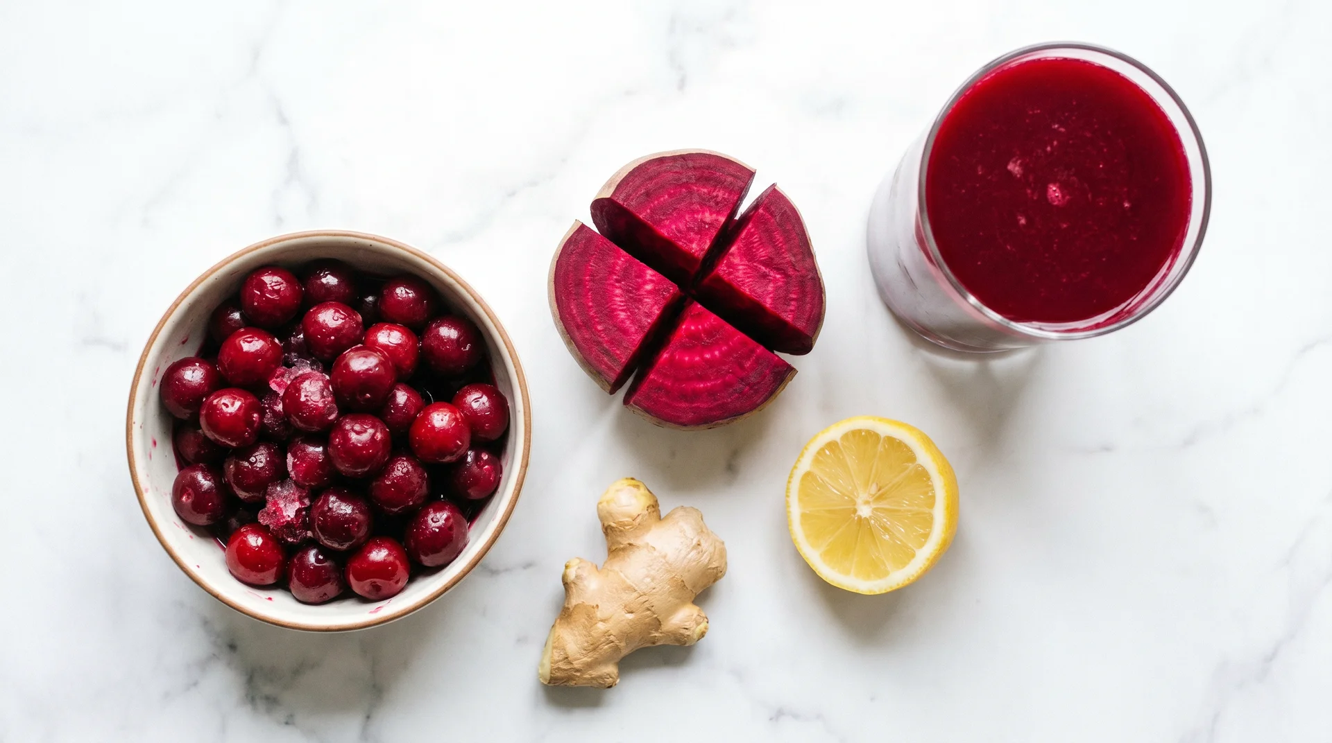 Joint pain juice ingredients showing tart cherries, beet cross-section, ginger and lemon on marble with deep red finished juice
