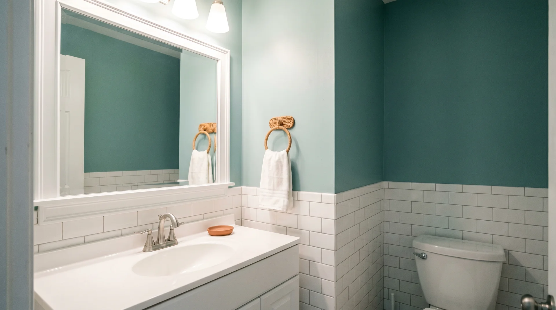 Sea salt painted bathroom with white tile and brass accents showing the color in controlled vanity lighting 